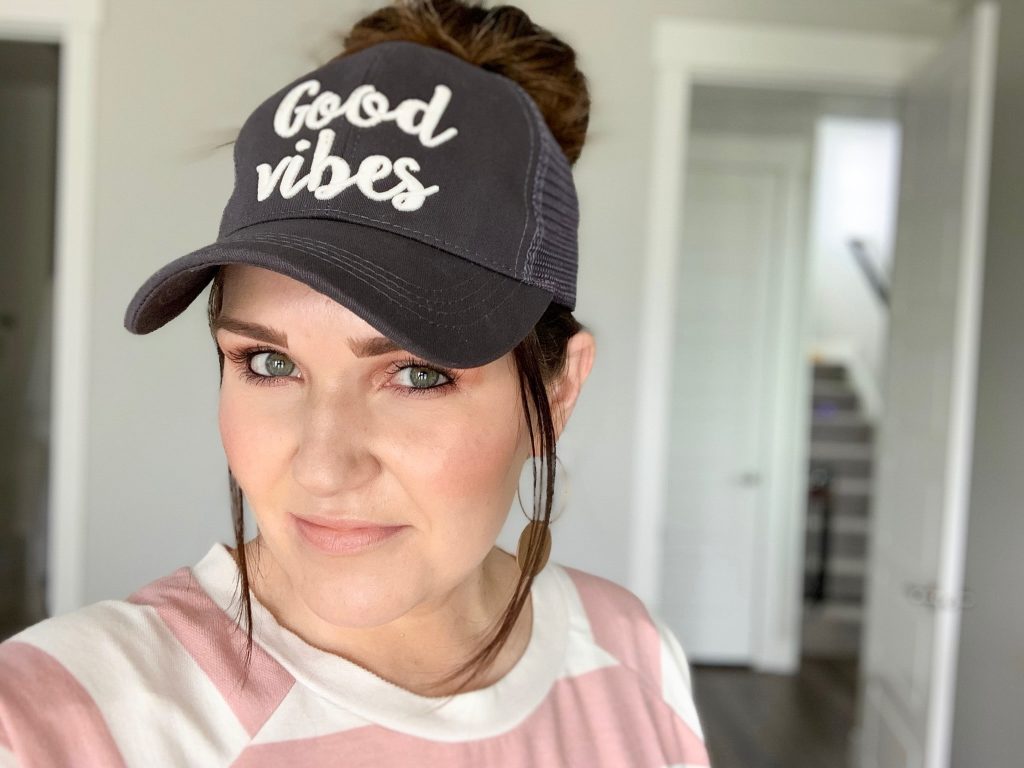 Messy Bun Hats - The best fifth day hair hack by Popular Utah Blogger and Top Maskcara Beauty Artist, Kelly Snider; image of woman wearing a Gray messy bun hat with the words "Good Vibes" written in white.