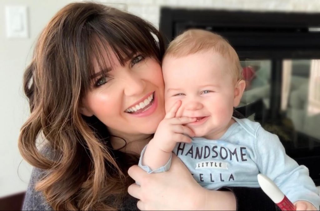 Kelly Snider with a smiling baby Popular Utah Blogger and Independent Maskcara Artist, Kelly Snider addresses MLM jobs for stay-at-home moms; image of smiling mom holding a smiling baby.