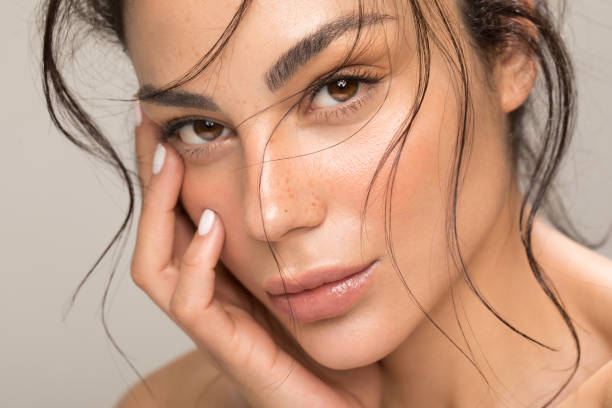 Close up studio shot of a beautiful brunette woman with glowing skin. Holding hands near her face.