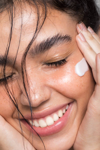 Close up studio shot of a beautiful woman with perfect skin, she applying cream with hydroxytyrosol on the cheek.